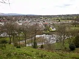 Photographie couleur d'un village situé le long d'une rivière, vus depuis une colline.