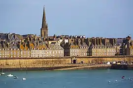 Vue de la ville depuis la mer, avec d'imposantes murailles au premier plan, et des maisons s'élevant derrière elles.