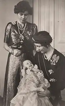 Photographie en noir et blanc montrant une femme assise portant un bébé avec, à sa gauche, une jeune femme debout.