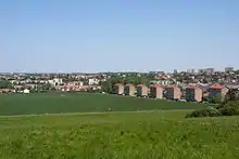 Alignement de petits immeubles collectifs en bordure d'une zone agricole en légère cuvette.