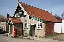 Petit bâtiment en bâtière dont un versant est prolongé par un appentis, avec un porche en bâtière sur le pignon