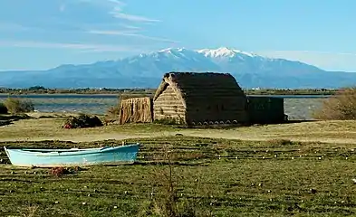 Maison traditionnelle de pêcheur sur le bord de l'étang, avec le massif enneigé du Canigou en arrière plan.