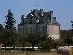 Photographie en couleurs d'un château à étage partiellement masqué par des arbres.