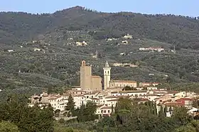 Photographie en couleurs représentant un village sur le flanc d'une colline. Les maisons ont une façade beige et des toits rouge ou rouille. Une église et un clocher surplombent le village.