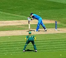 Devant son guichet qu'il protège, un joueur de cricket tente de dévier la balle avec sa batte.