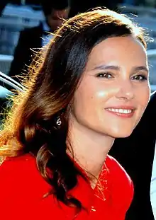  Photographie d'un visage féminin souriant vu de trois-quarts droit. Un vêtement rouge vif couvrant le buste est visible sur ce cliché.
