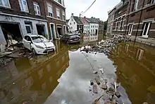 Une rue inondée, des débris émergeant de l'eau et plusieurs voitures sales en travers.