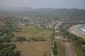 Photographie aérienne, où apparaît, au premier plan à droite, l'extrémité nord de la piste de l'aéroport Alcides-Fernández, et au second plan, au-delà du fleuve côtier Acandí, la petite ville d'Acandí.