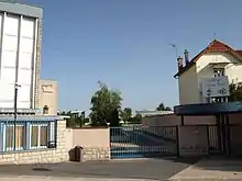 L'entrée du collège du Vieux-Port : une grille coincée entre deux bâtiments laisse apercevoir une cour de récréation et des arbres.