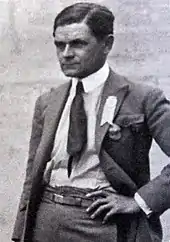 Photographie en noir et blanc d'un homme de trois-quarts en plan américain, brun, avec une main sur la hanche.