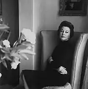 Photographie en noir et blanc d'une femme, l'air sérieux, assise sur un fauteuil.