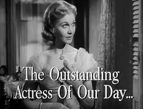 Image en noir et blanc d'une femme aux cheveux clairs et à la robe claire et sophistiquée, avec le texte "The Outstanding Actress of Our Day" en superposition.