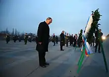 Photographie de Vladimir Poutine s'inclinant devant une gerbe de fleurs.