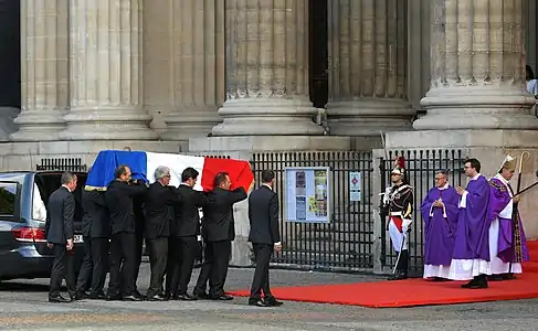 À l'entrée de l'église Saint-Sulpice, des officiers de sécurité de l'Élysée sous la présidence de Jacques Chirac portant le cercueil de celui-ci.