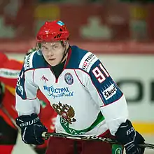 photographie d'un joueur de hockey sur glace avec l'équipement de l'équipe nationale russe, maillot blanc et casque rouge