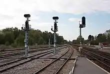 Vue de voies ferrées et de signaux lumineux (deux, à gauche, sont au rouge ; le troisième, à droite, est au vert), depuis un quai.