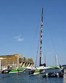 Vu de trois quarts avant, trimaran noir, vert et blanc amarré au ponton.