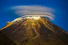 Une montagne arrondie avec un peu de neige au sommet et de nuages en forme d'anneau ou de couronne.