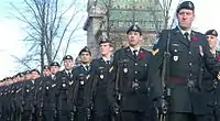 Photo de militaires en uniforme de parade tenant un fusil à l'épaule et défilant en rang à l'extérieur