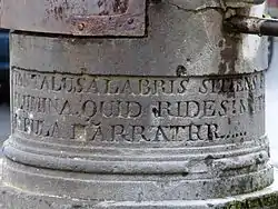 Détail de la base d'un pilier rond portant une inscription en latin apparaissant partiellement.