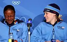 Photographie de deux femmes souriantes en conférence de presse, portant des survêtements bleu ciel.