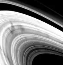 Gros plan sur l'anneau de Saturne, des tâches sombres contrastes avec l'apparence brillante de l'anneau.