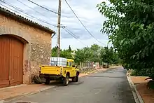 Une rue d'un hameau, avec un vieux pick-up jaune stationné devant une grange.