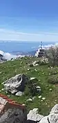 Le sommet du Grand Mont (croix à cheval sur la frontière) vu depuis l'Italie, avec le littoral de Roquebrune-Cap-Martin au second plan.