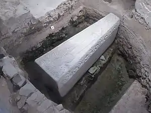 Sarcophage en pierre orné placé dans une cavité située sous une vitre.