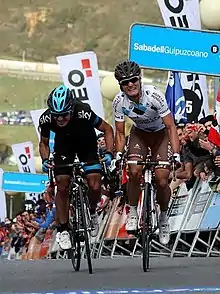 Photographie de deux cyclistes en plein effort, de face. À gauche, Henao en noir et bleu. À droite, Betancur en blanc et marron.