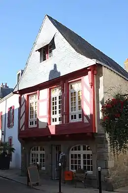 Vue d’une maison en granit, pans de bois rouges en façade, toit en ardoises.
