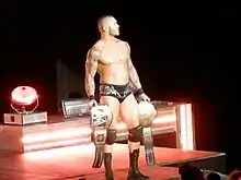 Randy Orton en slip entrant sur le ring avec une ceinture dans chaque main.