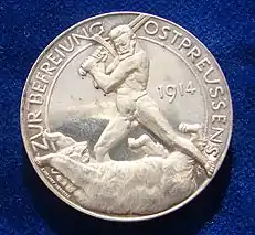 Le revers d'un médaillon d'argent allemand de la Première Guerre mondiale célébrant la libération de la Prusse orientale en 1914 par Paul von Beneckendorff und von Hindenburg, se référant à la bataille de Tannenberg. C'est une représentation du général Hindenburg nu combattant un ours russe avec son épée.