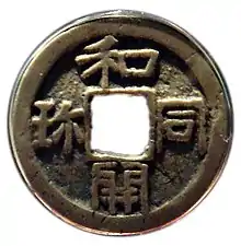 Photo couleur d'une pièce de monnaie ronde, avec un trou de forme carrée en son milieu.