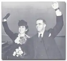 photo noir et blanc d'un couple au départ faisant des grands gestes d'au revoir