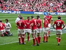 Arrêt de jeu. Regroupement des avants gallois devant, au fond les supporters gallois sont vêtus de rouge.