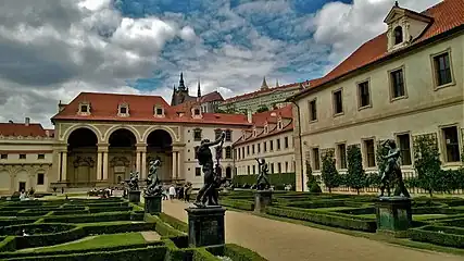 Un jardin à la française, orné de statues, entouré par plusieurs corps de bâtiments Renaissance, en pierre de taille claire, aux toits de tuiles. La cathédrale sur une hauteur à l'arrière plan.