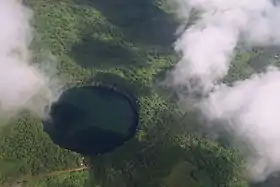 Photographie aérienne montrant un lac circulaire entourée de végétation et d'une route passant à côté.