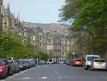 Une grande avenue bordée d'immeubles en pierre grise sur la gauche et d'arbres sur la droite