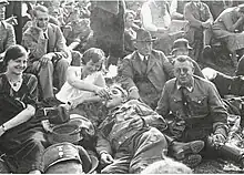 Photographie en noir et blanc d'hommes et de femmes tant en civil qu'en uniforme, assis ou allongés sur le sol.