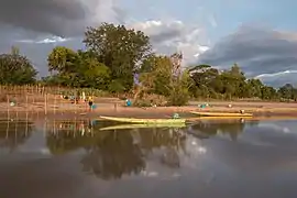 Réflexion (optique) sur l'eau d'une berge avec des arbres et deux pirogues au coucher du soleil sur l'île de Don Puay à Si Phan Don. Décembre 2017.