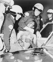 Un groupe de policiers blancs tenant et étouffant un homme noir torse nu pour le faire entrer dans une voiture.