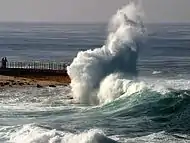 Une lame se brisant et déferlant sur une jetée.