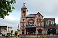 Photographie d'un grand bâtiment aux tons beiges et orangés. Il a un clocher et un style ancien.