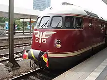 Un train rouge et or orné d'un pavillon allemand en quai.