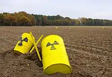 Photographie de deux fûts jaunes au milieu d'un champ. Sur ceux-ci est peint le symbole de la radioactivité.