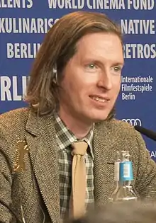 Photographie d'un homme blond assis à une table de conférence.