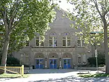 Un grand bâtiment en briques grises entouré d'arbres.