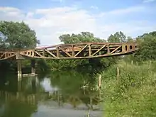 Le pont de Vacherauville date de 1944, il provient des travées du port Mulberry ayant servi au débarquement de 1944. C’est un pont historique, il n’en reste plus beaucoup en France, un morceau d’Histoire de la Seconde Guerre Mondiale là où la Première a fait des ravages. Ce pont a permis aux paysans vacherauvillois de rejoindre l’autre bord du canal de la Meuse. Ces deux travées ont été apportées ici, à Vacherauville, en 1960.