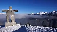 Paysage montagneux avec de la neige. Au premier plan à gauche, un construction de pierres rectangulaires assemblées pour avoir une forme humaine.